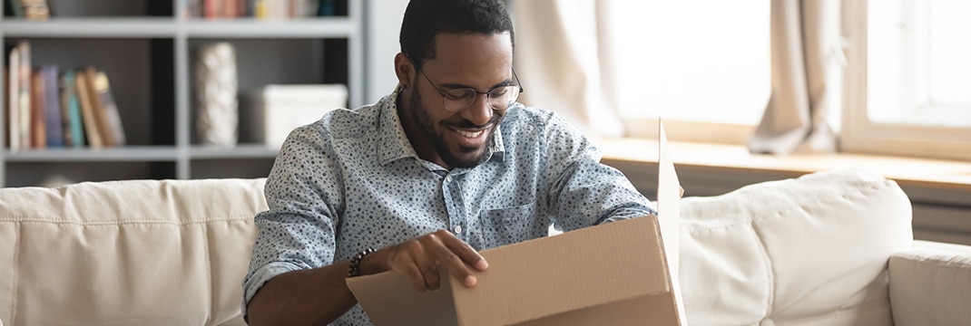 Een lachende man zit op een bank en opent een pakketje