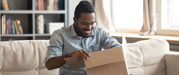 Een lachende man zit op een bank en opent een pakketje